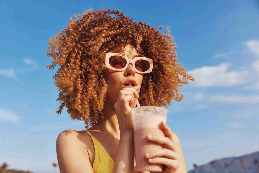 woman with curly hair enjoying a smoothie on a sun 88Z62G9 1