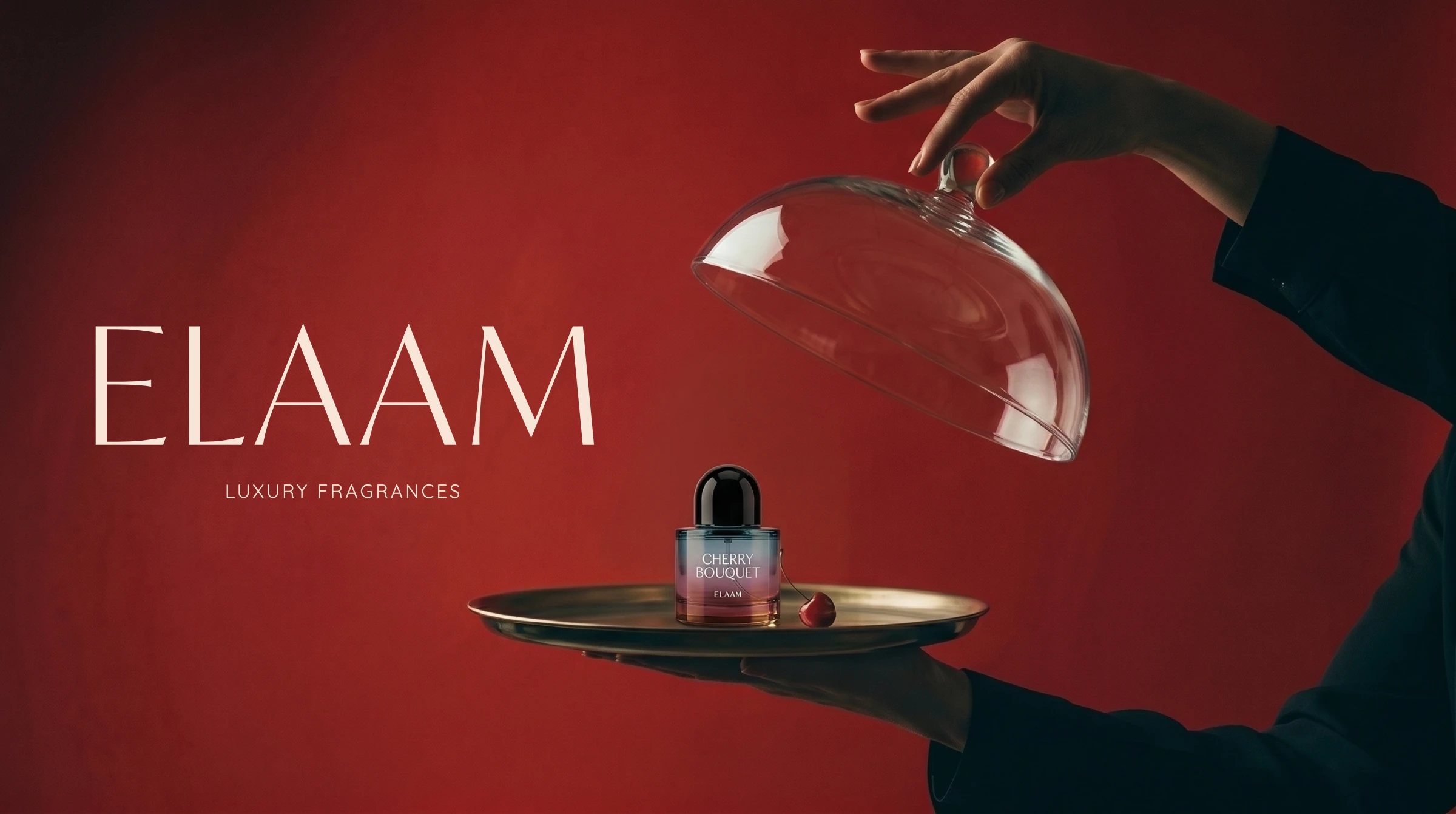 Hand lifting a glass cloche from an Elaam Cherry Bouquet bottle on a gold tray